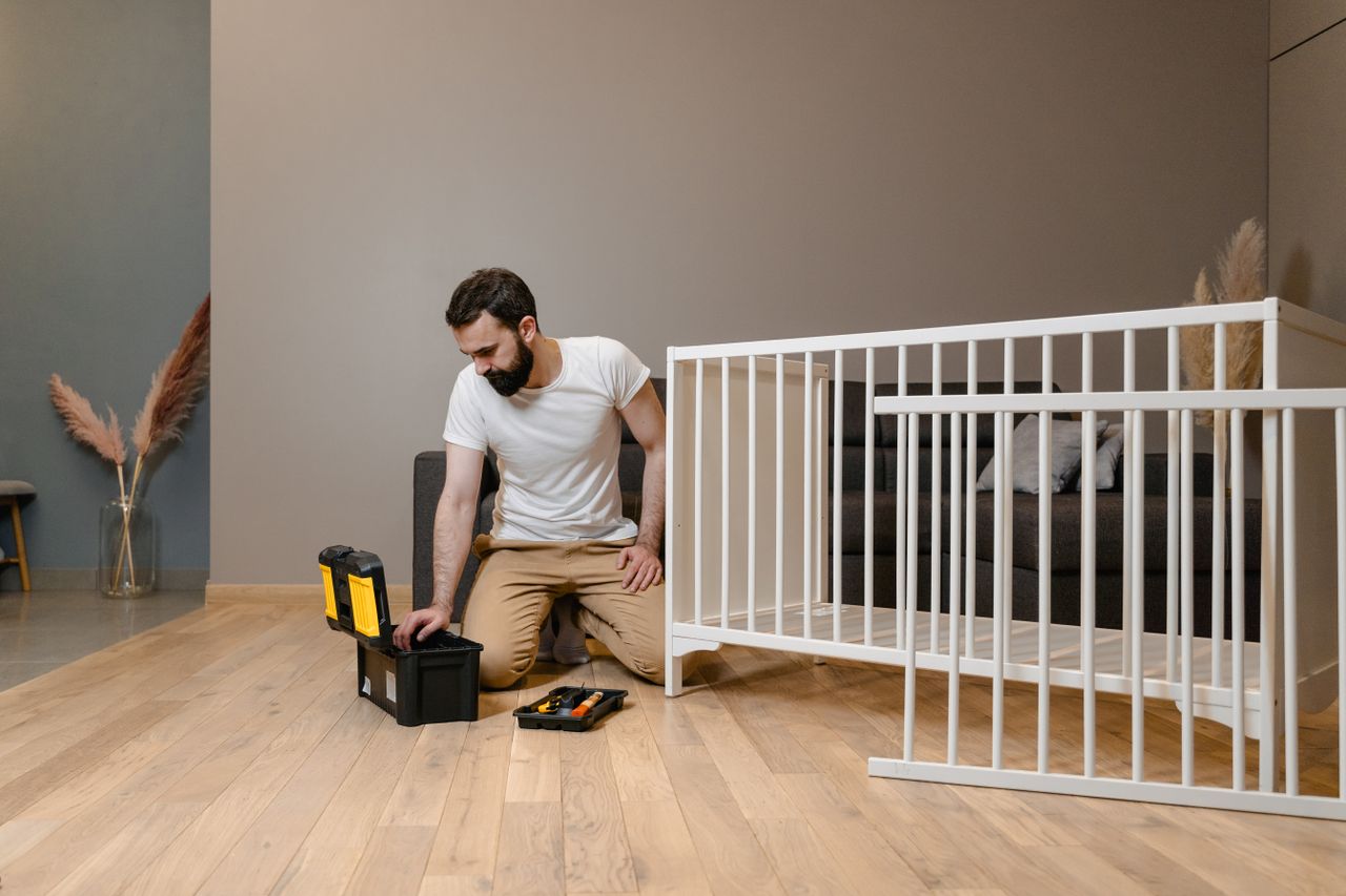 Offerings A man assembling a white crib indoors with tools, focusing on DIY and home care.