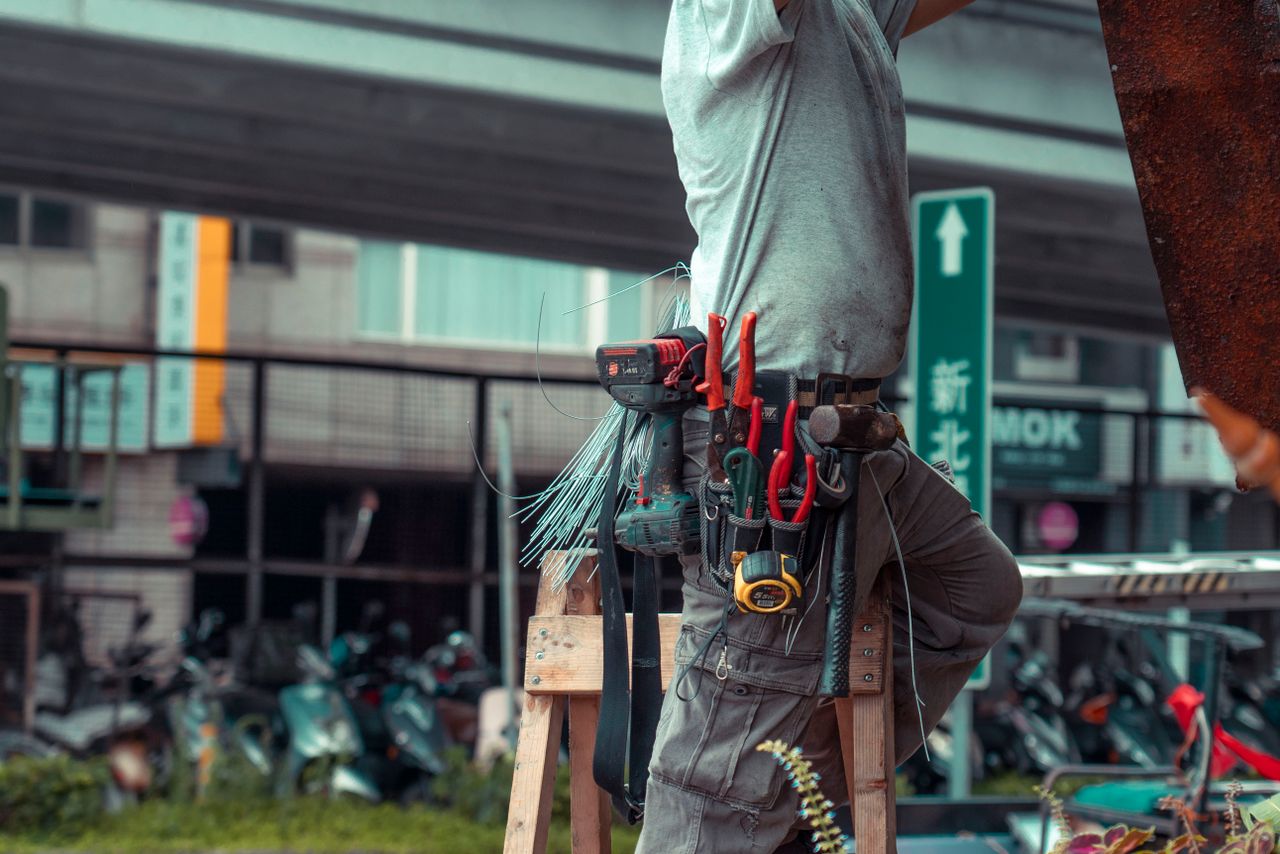Offerings Handyman standing on a ladder with tool belt, repairing outdoors with visible tools.